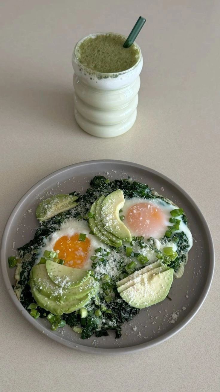 Eggs, spinach and avocado on a plate beside a green smoothie.